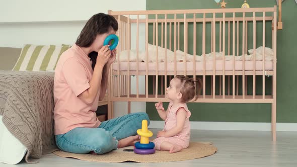 Mom and Daughter Play Toys at Home While Sitting on the Floor in the Bedroom