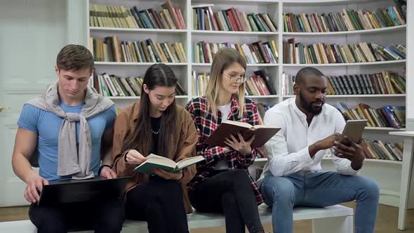 Multiracial Students Sitting on the Bench in Library and Preparing for Exams Using Books