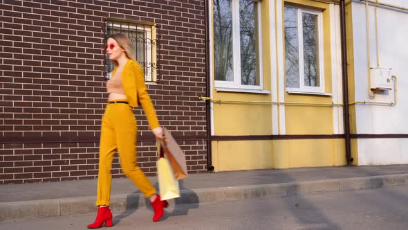 One Young Caucasian European Girl Shopaholic Walking Along the Street with Purchases in Packages. 