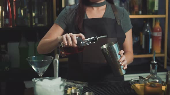 Dolly shot of female cocktail waiter pouring alcohol liquid in shaker in nightclub