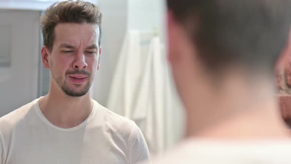 Upset Young Man Looking at Face in Mirror