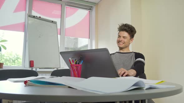 Young Male College Student Smiling, Typing on His Laptop