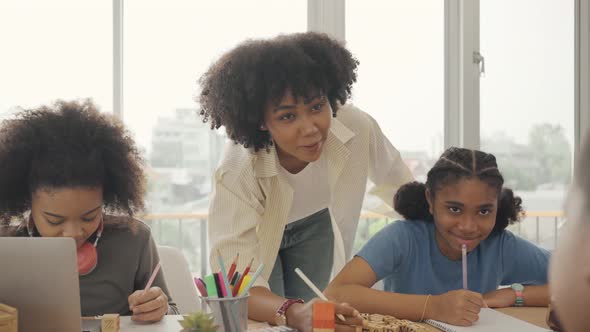 African American female teacher standing with pupils teaching writing lesson in modern classroom.