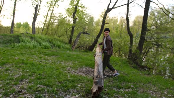 Slow motion 2x young man carry large log through the forest for sitting near the fireplace, side