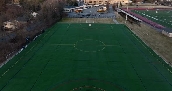 School athletic field and campus. Aerial tilt up reveals school building and school bus fleet. Ameri