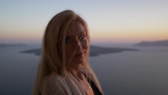 Blond woman smiling and watching sunset over island Santorini Greece