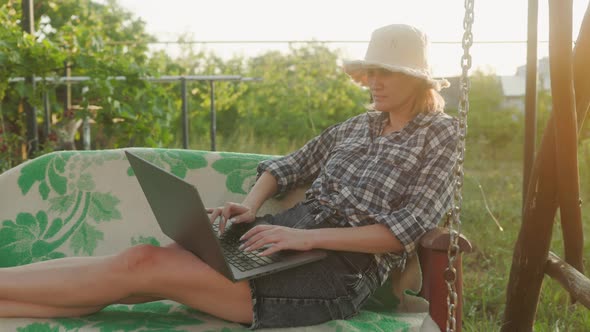 Young adult woman working outdoors in her garden with laptop. Freelancer using laptop