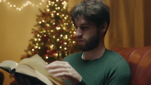 Boy reads book beside Christmas tree