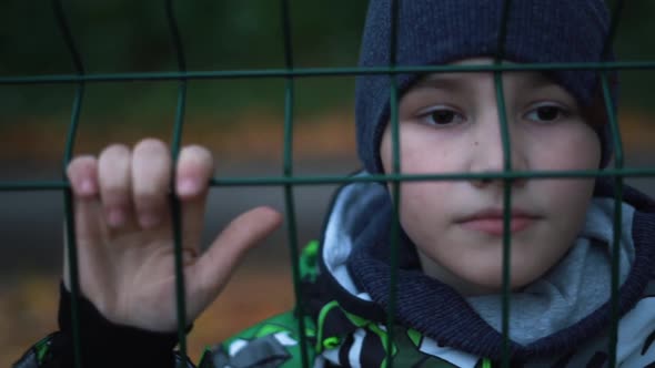 Lonely Unhappy Miserable Young Boy Behind and Clinging to Fence