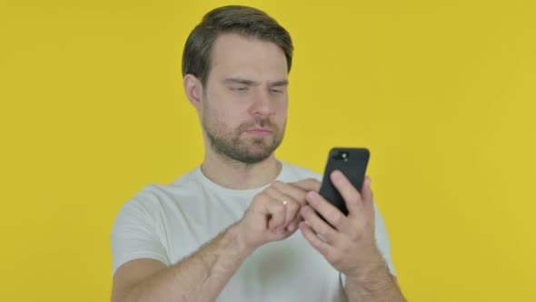 Young Man Browsing Smartphone on Yellow Background