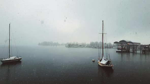 Snow falling over Maggiore lake and anchored sailing boat and ferry, Italy