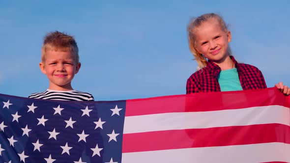 Portrait of Blonde Boy and Girl with National USA Flag Outdoors Over Blue Sky on Sunset at Summer