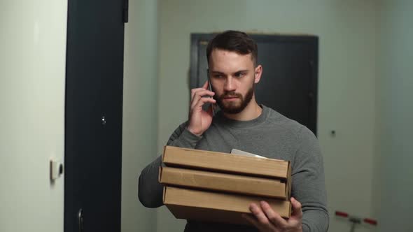 Delivery Man Standing at Door of Customer Apartment with Boxes of Pizza and Calling Client on Phone