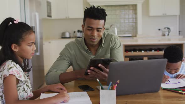 African american father, daugher and son sitting at kitchen table doing homework