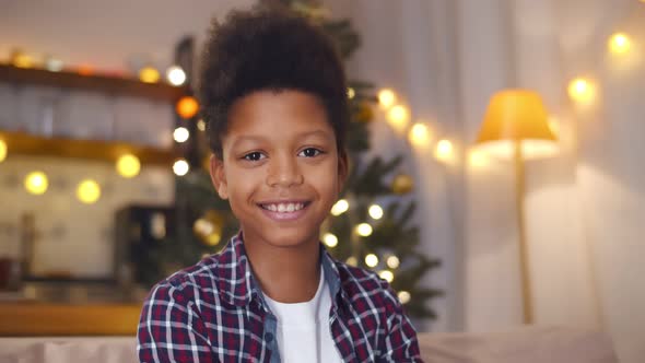 Portrait of African Teen Boy Sitting on Sofa and Smiling at Camera on Christmas Eve