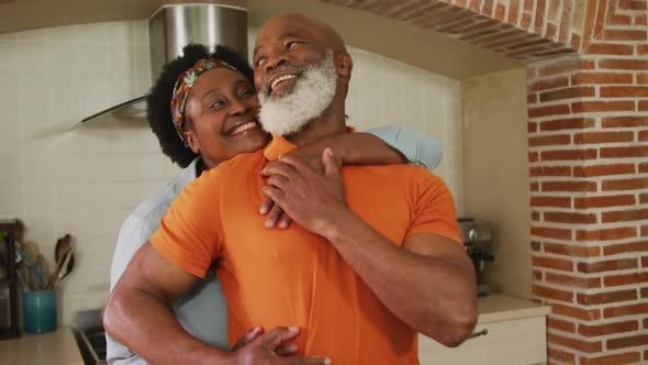 African american senior couple embracing each other in the kitchen at home