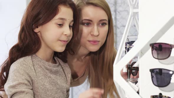 Cute Little Girl Choosing Sunglasses with Her Older Sister at the Store