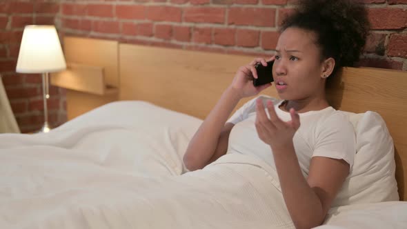 Angry African Woman Talking on Smartphone in Bed