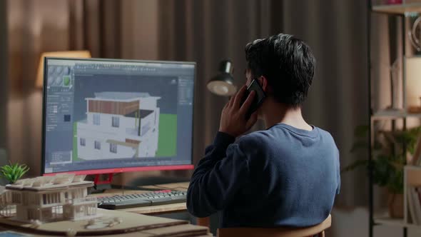 Asian Male Engineer Talking On Smartphone While Designing House On A Desktop At Home