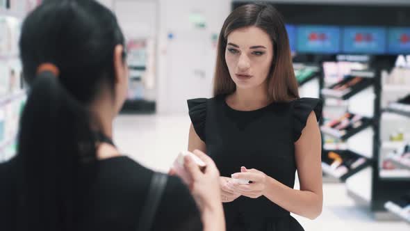 Front View of Young Woman Talking with Shop Assistant in Cosmetics Store