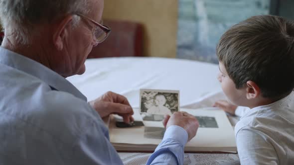 Friendly Grandfather with His Beloved Grandson Shows Photos of Youth Rejoicing in Memories of Youth