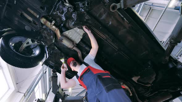 Auto Mechanic Uses His Flashlight to Inspect a Vehicle From Below