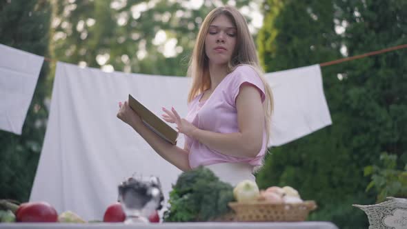 Side View Confident Slim Young Housewife Reading Recipe Looking at Ingredients on Table on Backyard