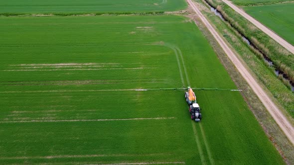 Aerial birdseye view of tractor spraying pesticide and fertilizer on the green field in overcast sum