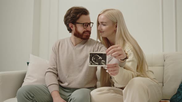 Cheerful Millennial Caucasian Wife Hugging Her Husband and Holding Ultrasound Picture of Their