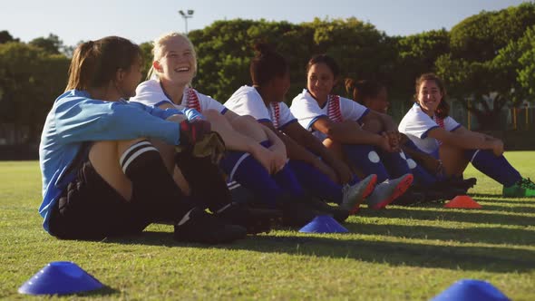 Female soccer team sitting on the ground while talking on soccer field. 4k