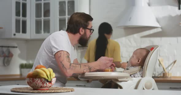 Young Couple Feeding Their Baby in Kitchen