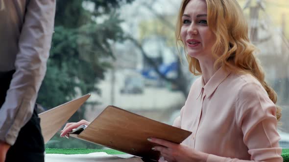 Happy Woman Talking with Waiter, Sitting in the Table of a Cafe