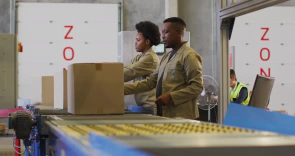 African american male and female workers with boxes on conveyor belt in warehouse