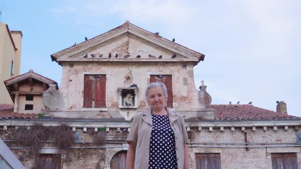 Elderly Woman Stands Against Old Abandoned Building