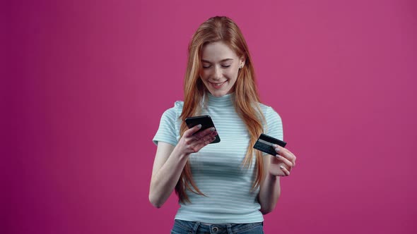 The Happy Young Woman with the Phone and the Card in Her Hand is Shopping Online in a Blue Casual