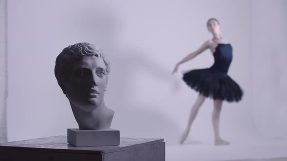 Young Woman Ballerina in Black Dress Training a Head of Greek Sculpture on the Foreground in Playing