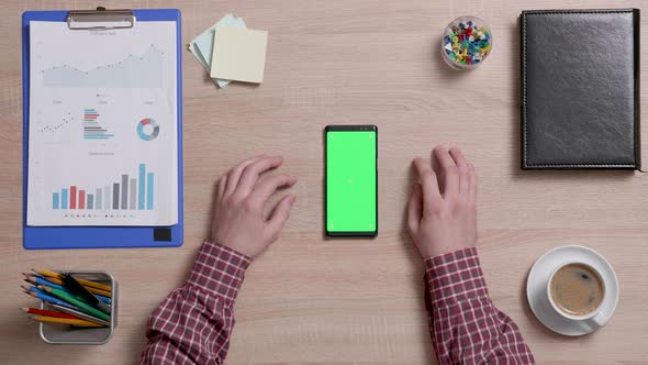 Top View of a Man's Hands Touch the Center of a Green Screen on a Smart Phone