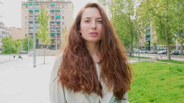 Woman with long hair standing in city, looking at camera