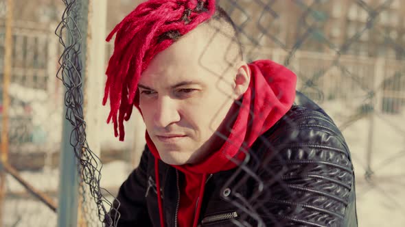 Stylish Man with Red Dreadlocks Leaning on Metal Fence