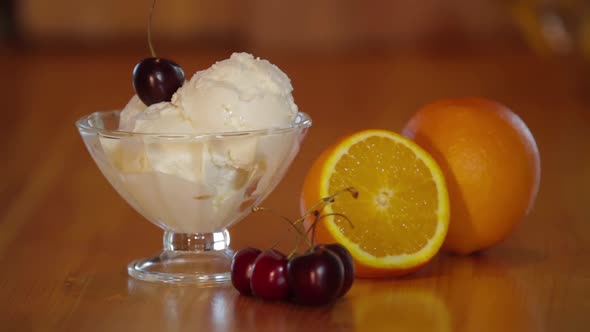 Cherry on Top of Ice Cream Scoops. Ice Cream with Cherrys in a Glass Bowl and Orange on a Wooden