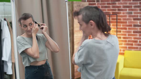 Woman Looking in the Mirror Shaves Off Long Hair with a Trimmer While Standing at Home in the Room