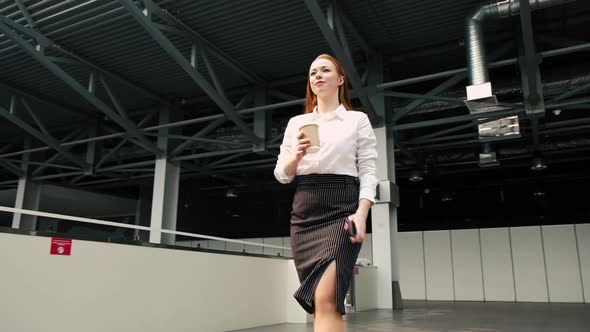 female leader walks through lobby of business center with a phone and cup coffee
