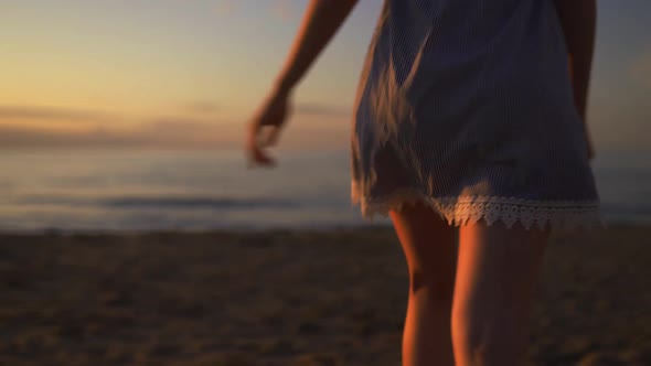 Close Backside View of Young Woman Running at Sea on the Beach Wearing Blue Summer Dress During