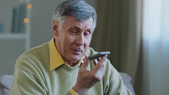 Mature Greyhaired 60s Man 70s Senior Old Male at Home Hold Smartphone Speak Loud to Phone Microphone