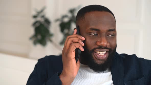 Closeup Portrait of Cheerful and Smiling AfricanAmerican Guy Chatting on the Smartphone