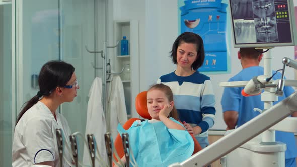 Child Using Finger To Point Affected Tooth While the Dentist Talking with Mother