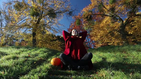 woman in coat and with pumpkin sits on stair in autumn park