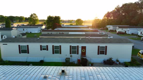 Low drone flyover of mobile homes. Sunburst on lens from sunset in spring. Mobile home park for low