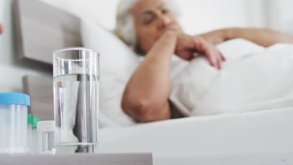 Sick african american senior woman drinking water while lying on the bed at home