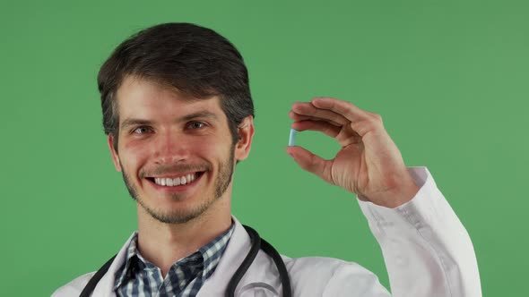 Cheerful Male Doctor Smiling Holding Blue Pill on Green Background